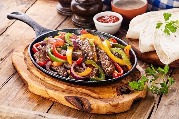Fajitas de bœuf Servies avec des haricots frits (frijoles) et des tortillas de maïs. Minimum de 2 personnes